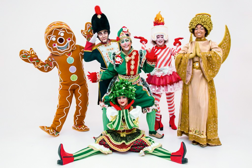Seis pessoas vestidas de personagens de Natal (biscoito, anjinho, árvore etc) posam em um fundo branco