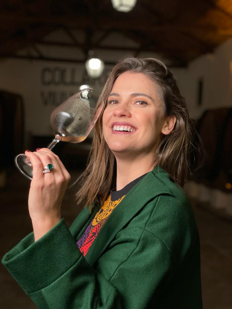 A apresentadora Elisa Veeck posa sorrindo e segurando uma taça de vinho
