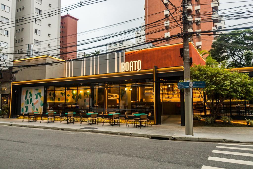 Fachada de bar com mesas na calçada e ambiente envidraçado