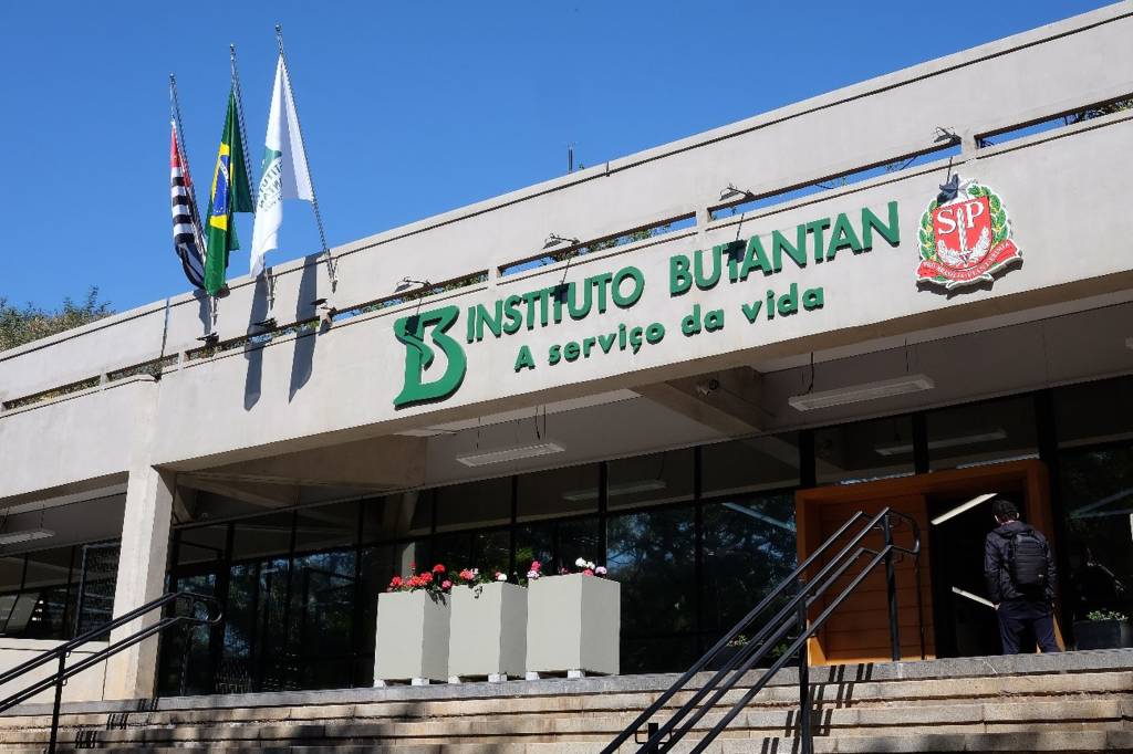 Imagem mostra fachada de prédio com o texto em verde "Instituto Butantan: à serviço da vida". É possível ver escadas e duas bandeiras no alto da fachada.