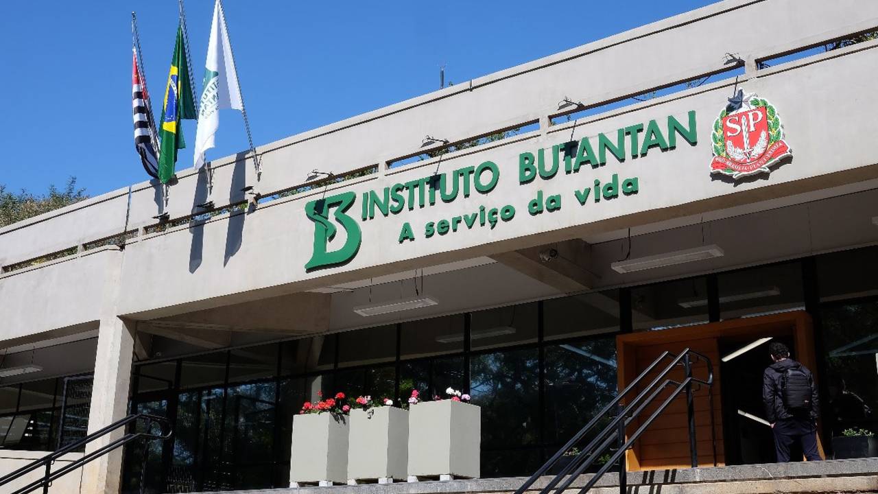 Imagem mostra fachada de prédio com o texto em verde "Instituto Butantan: à serviço da vida". É possível ver escadas e duas bandeiras no alto da fachada.