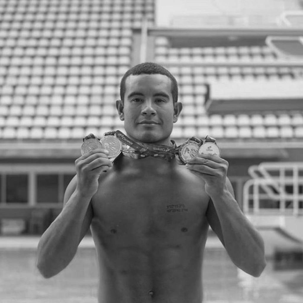 Ian aparece sem camisa, diante de piscina, segurando medalhas de competições