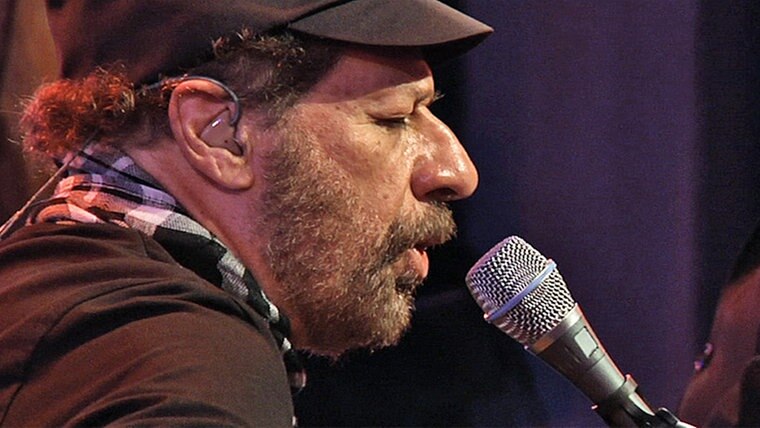 Imagem mostra homem de perfil com um microfone em sua frente, cantando.