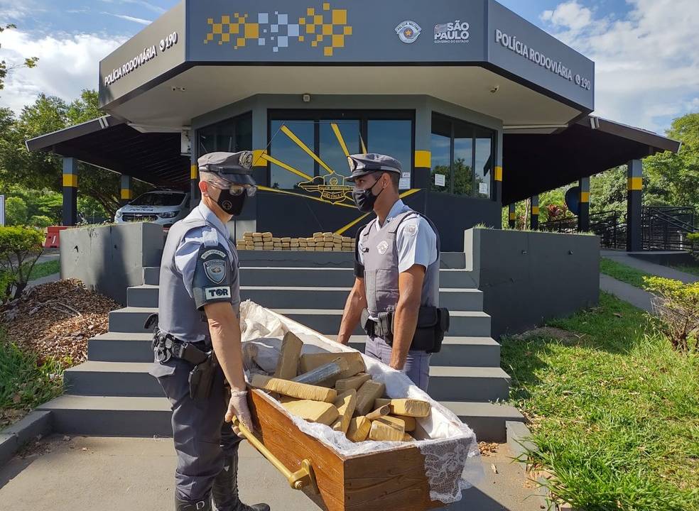 Imagem de dois policiais carregando um caixão de madeira com pacotes de maconha dentro
