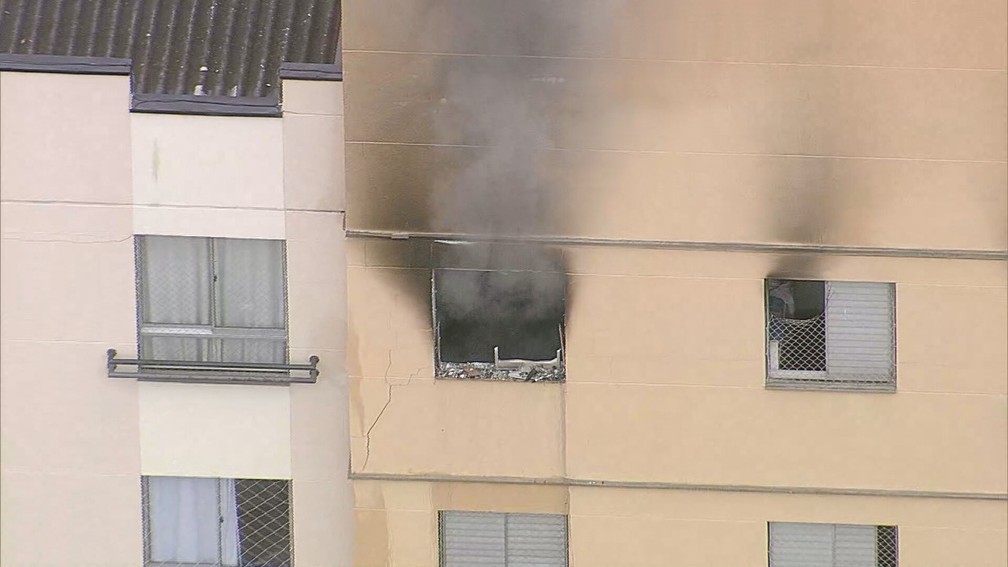 Foto do prédio pegando fogo. A fumaça sai por duas janelas.
