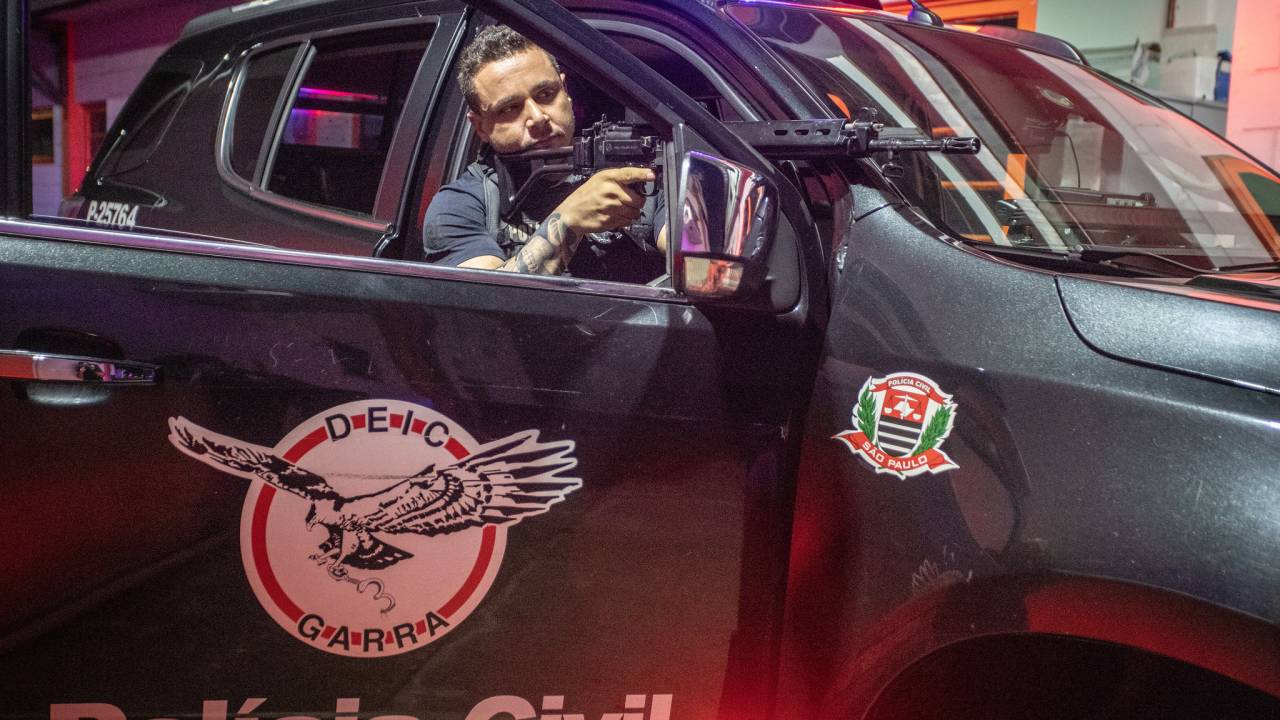 Homem segura fuzil apoiado em janela de viatura policial