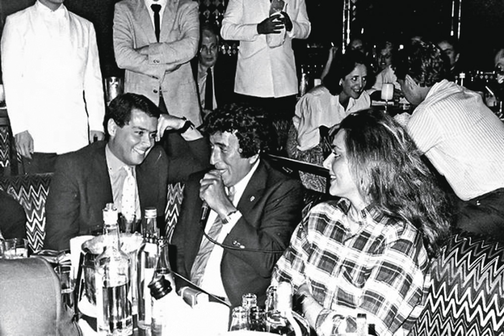 Imagem mostra dois homens e uma mulher sentados em uma mesa, conversando.