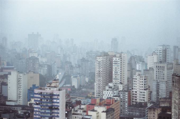 Imagem mostra horizonte de prédios sob tempo nublado e chuva.