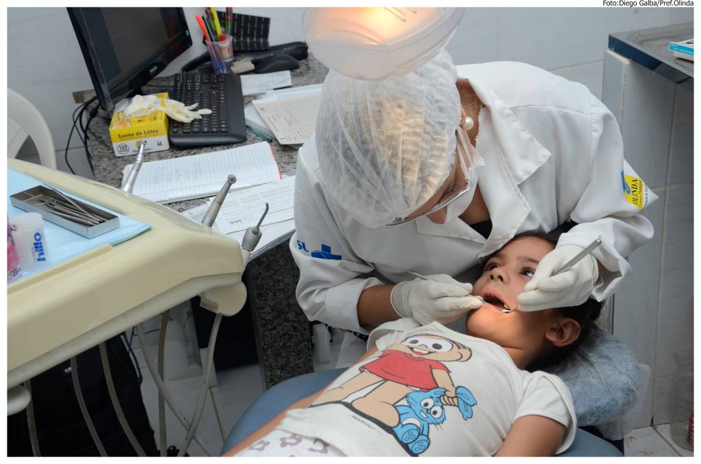 Imagem mostra criança em consultório de dentista, sendo atendida por uma dentista.