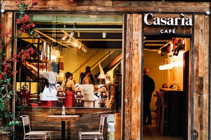 Fachada do Casaria Cafè com detalhes em madeira e uma mesa e duas cadeiras ao ar livre perto de flores de cor rosa