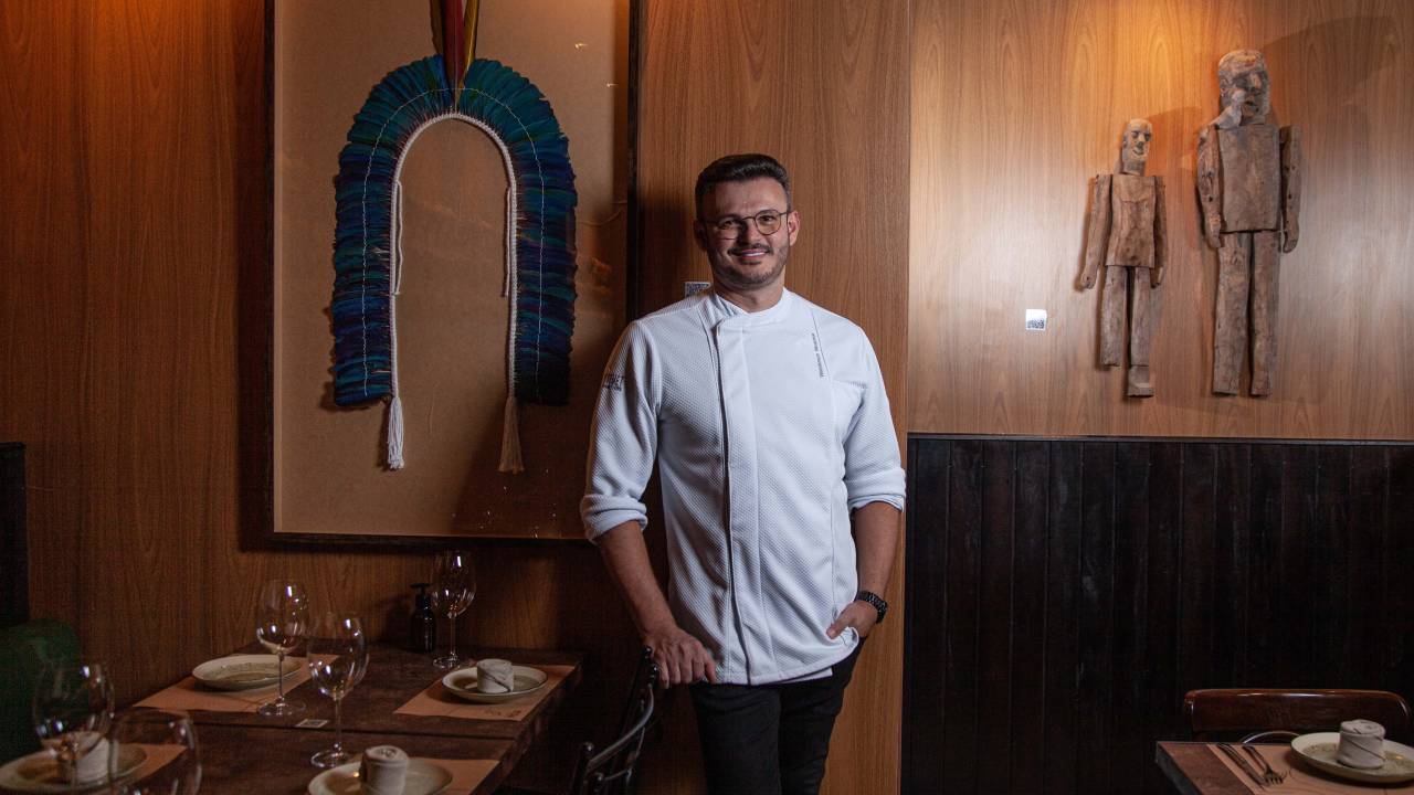 Chef do restaurante posa em frente à parede de madeira decorada por um cocar