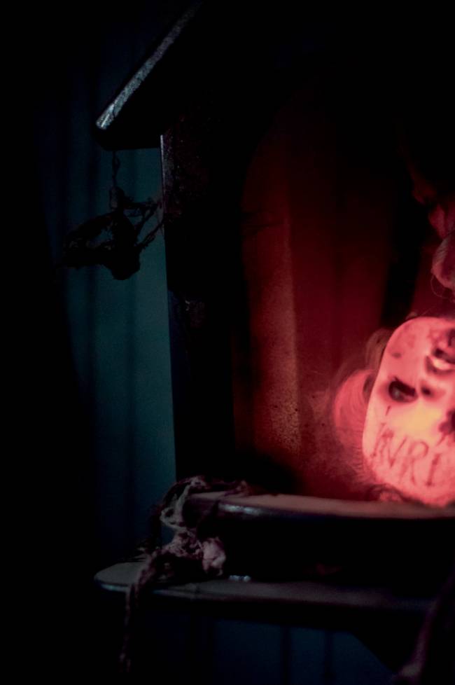 Imagem mostra cabeça de bebê iluminada por luz amarela, invertida e apoiada em um móvel de um quarto escuro.