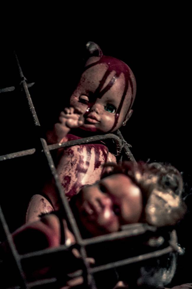Imagem mostra boneco de bebê ensanguentado em jaula enferrujada.