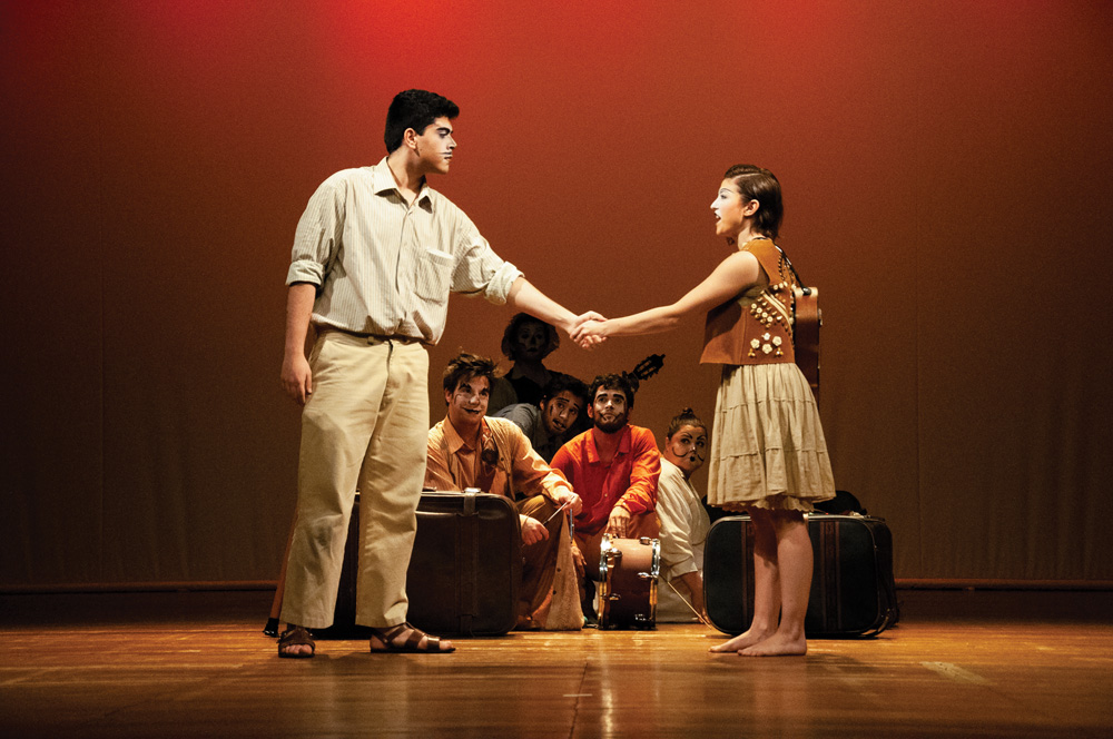 Dois atores, um homem e uma mulher, interpretam retirantes nordestinos. Eles aparecem em destaque e apertam a mão um do outro.