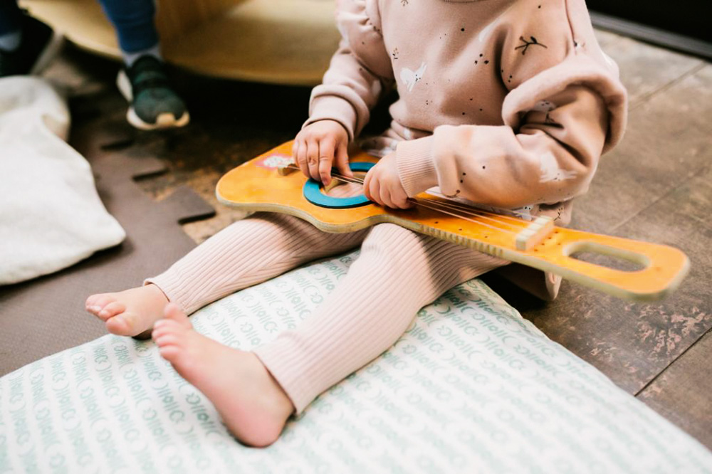 Foto de uma criança pequena manuseando um violão de brinquedo.