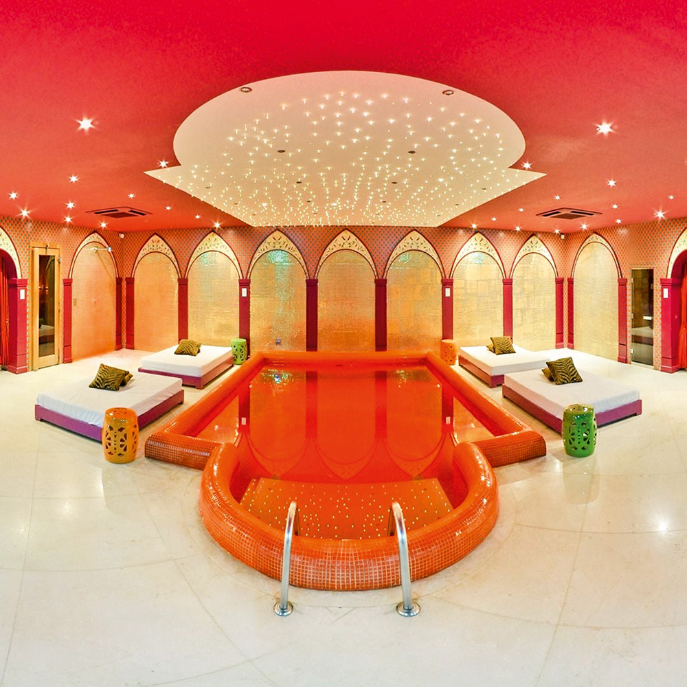 Imagem mostra espaço com uma piscina vermelha ao centro e teto vermelho. As paredes tem detalhes dourados.