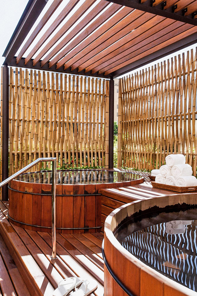 Imagem mostra estrutura de bambu sobre duas jacuzzis de madeira. Um montinho de toalhas brancas está entre as jacuzzis.