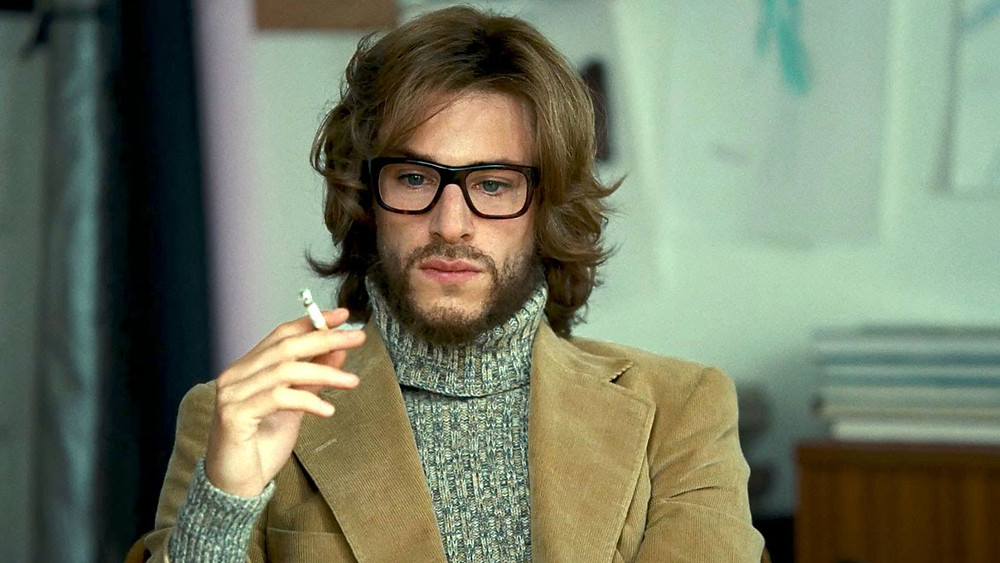 O ator Gaspard Ulliel, de óculos e blazer, segura um cigarro