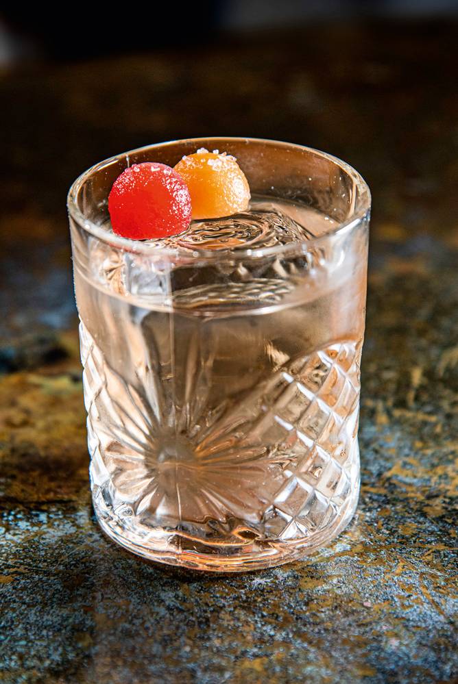 Drinque incolor servido em copo baixo e de fundo redondo decorado por duas bolinhas comestíveis e coloridas