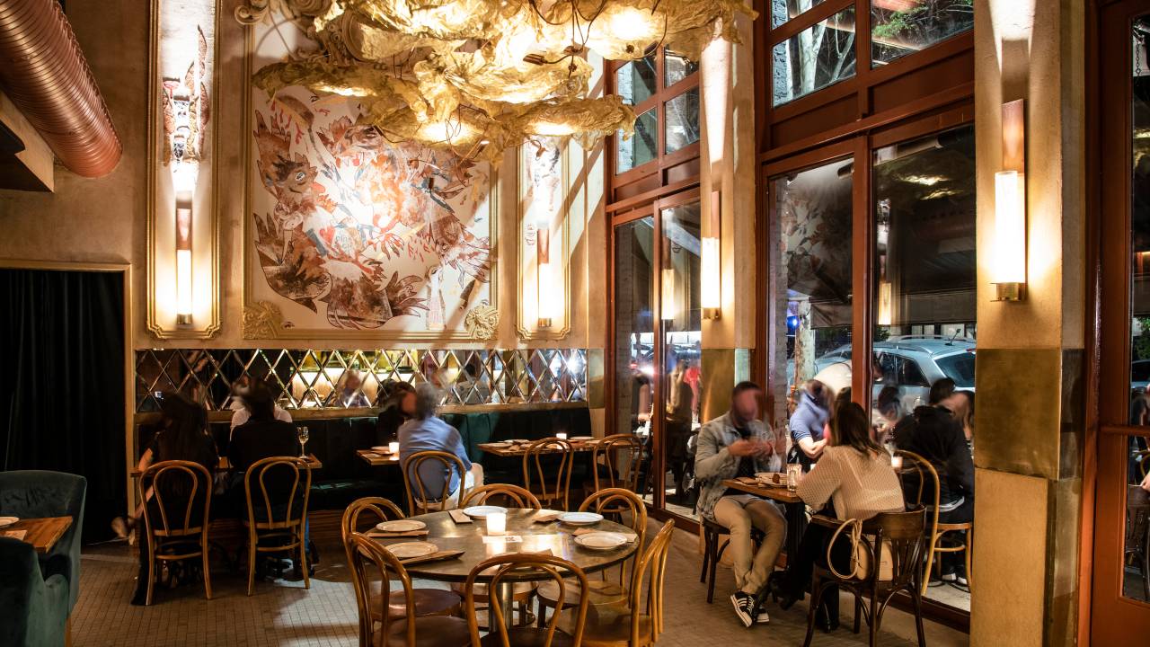 Ambiente de bar bem iluminado com detalhes em dourado e mesas e cadeiras de madeira