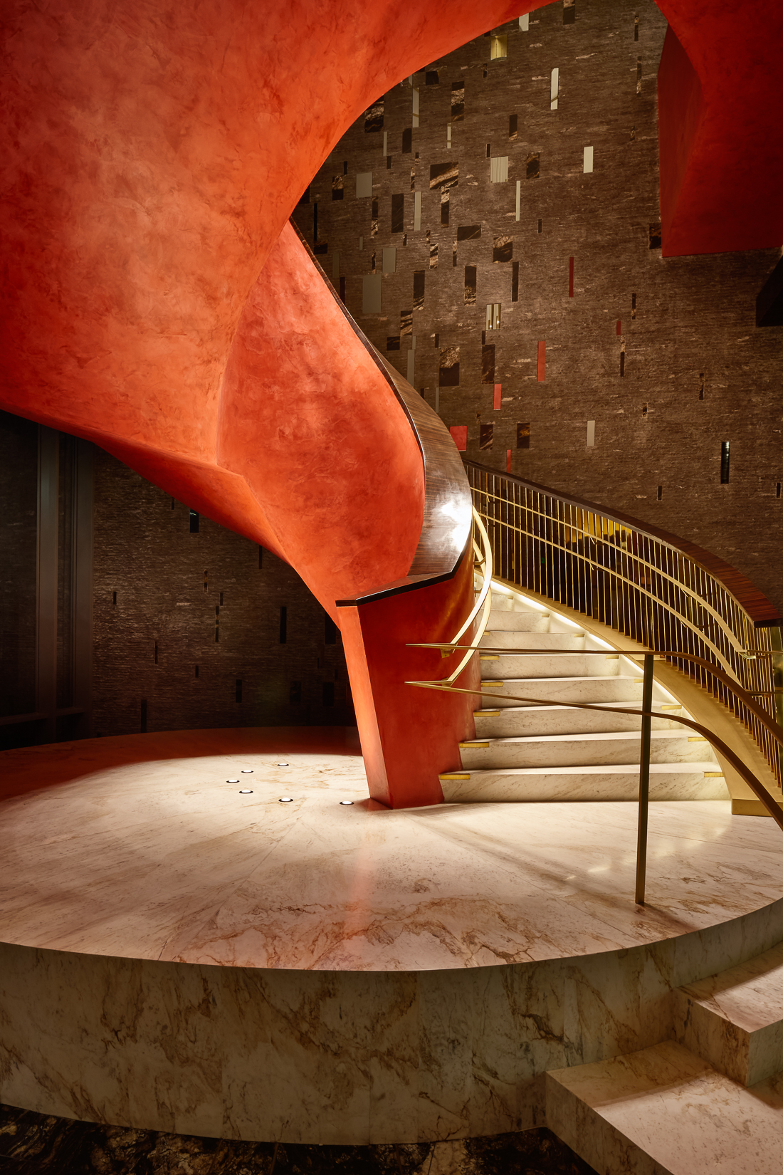 Escada em espiral de mármore com estrutura em vermelho com detalhes em dourado.