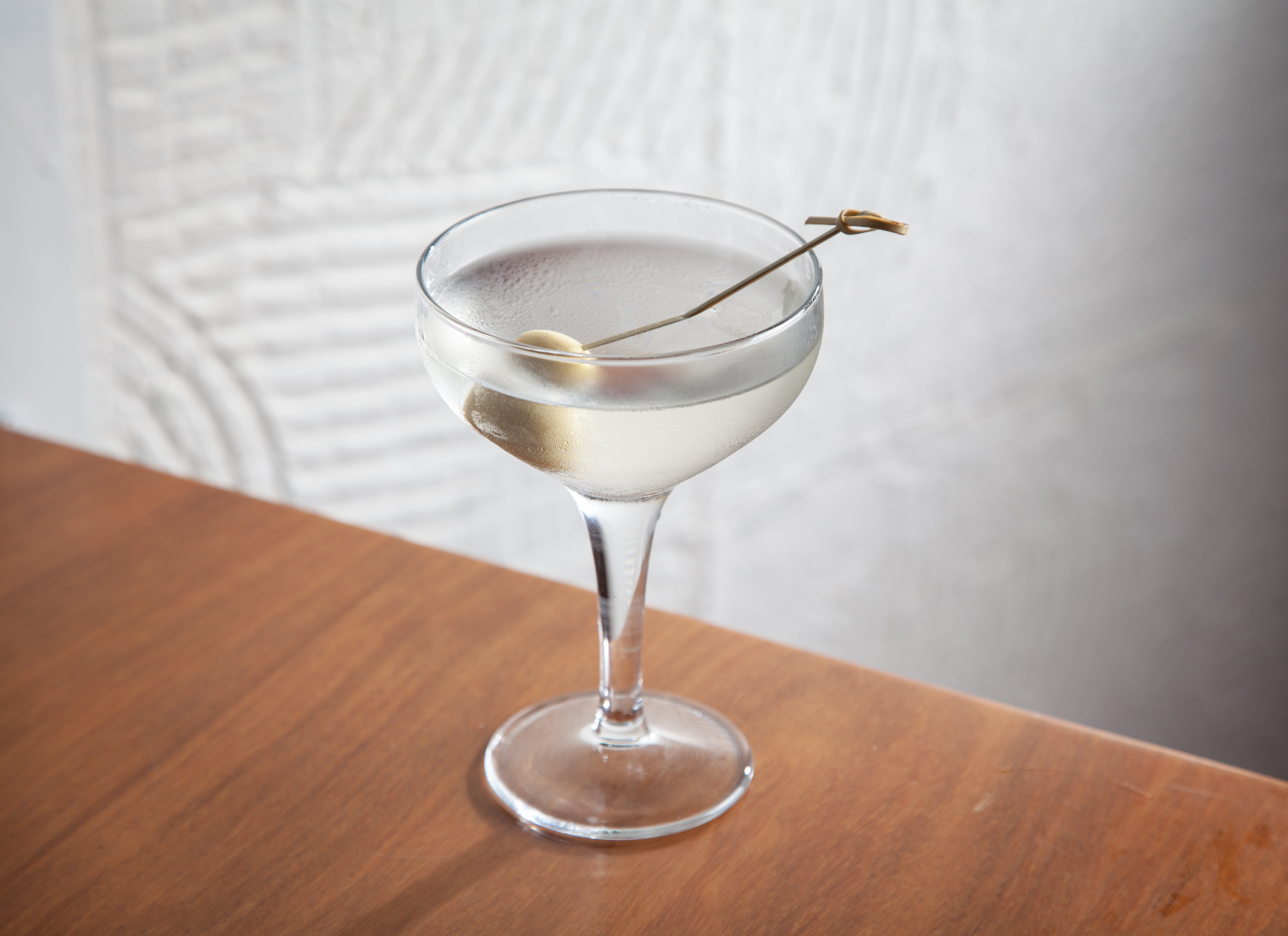 Drinque incolor servido em taça de martini junto de uma azeitona verde espetada em um palito