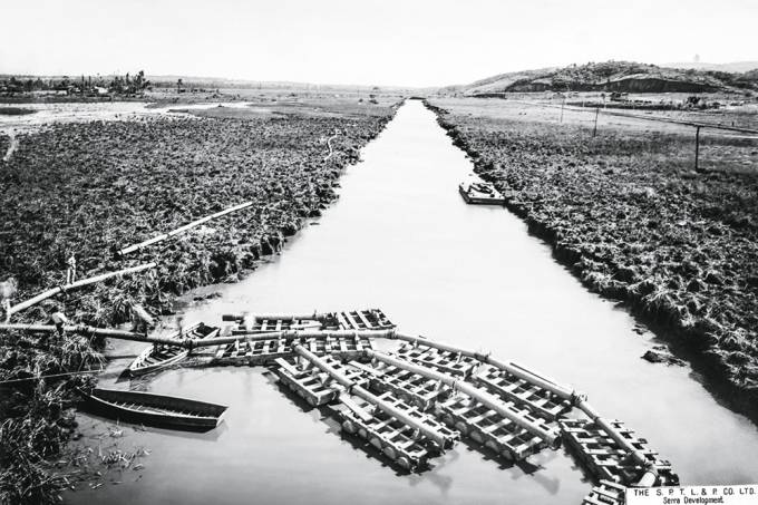 Imagem em preto e branco mostra rio entre margens de grama.