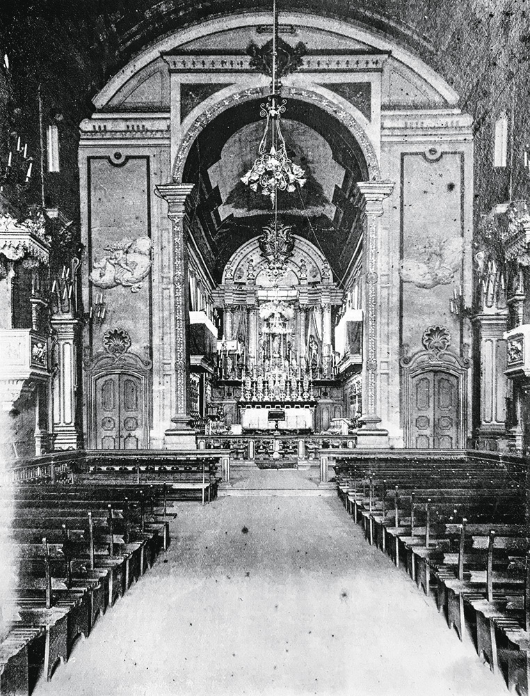 Imagem em preto e branco mostra altar de igreja, ao fundo, e corredor entre bancos ao centro.