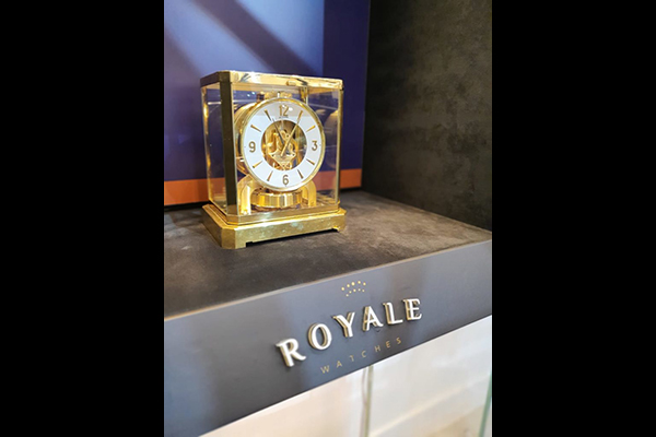 Imagem mostra, à esquerda, bancada com relógio cenográfico e, no balcão escrito 'Royale Watches'