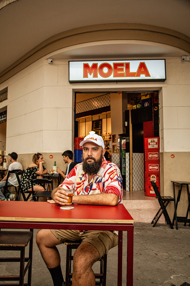 Rômulo Morente senta em mesa de madeira pintada na cor vermelha em frente ao Moela