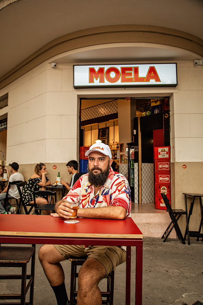 Moela Rômulo Morente senta em mesa de madeira pintada na cor vermelha em frente ao Moela