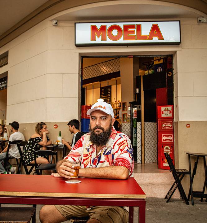 Rômulo Morente senta em mesa de madeira pintada na cor vermelha em frente ao Moela