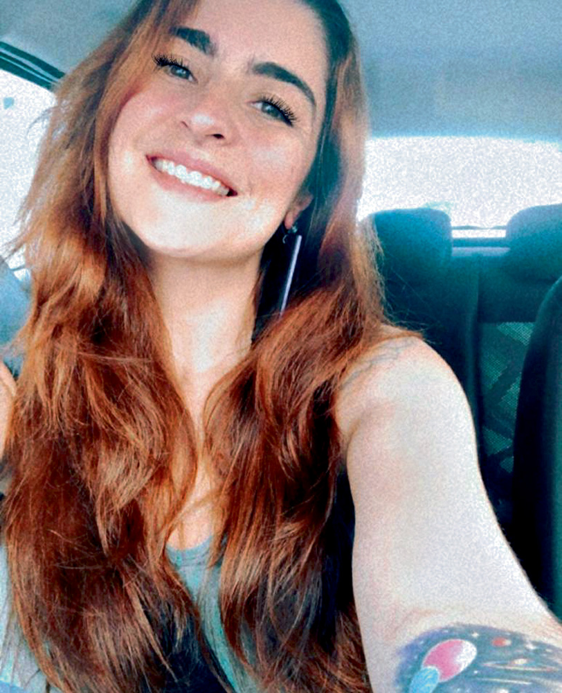 Imagem mostra mulher de cabelo ruivo dentro de carro, sorrindo para a câmera.