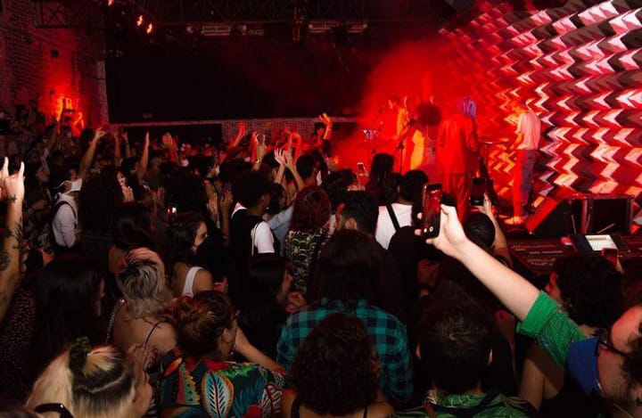 Imagem mostra multidão de pessoas em frente a palco iluminado por luz vermelha.