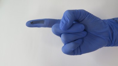 Imagem mostra mão com luva de borracha e, na ponta do dedo indicador, três faixas horizontais grudadas, responsáveis pela análise dos alimentos