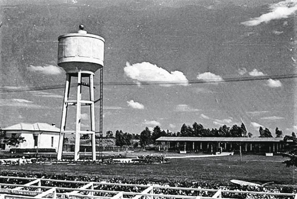 Imagem mostra campo com caixa d'água branca alta e uma estrutura ao fundo.