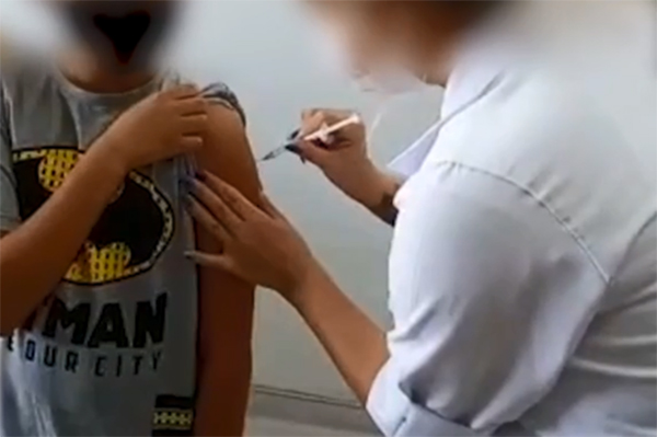 Imagem mostra criança com manga de camiseta levantada e enfermeira fingindo aplicar vacina contra a Covid-19