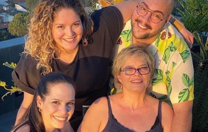 Foto mostra Cíntia e seus três filhos: Vivian, Tiago e Lígia. Todos são brancos, Vivian tem cabelos escuros e lisos e Lígia cabelos loiros e cacheados. Eles sorriem para a foto.