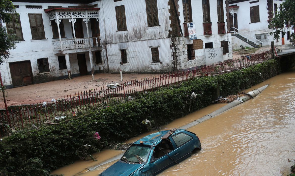 A imagem mostra alagamento em rua de Petrópolis com carro submerso