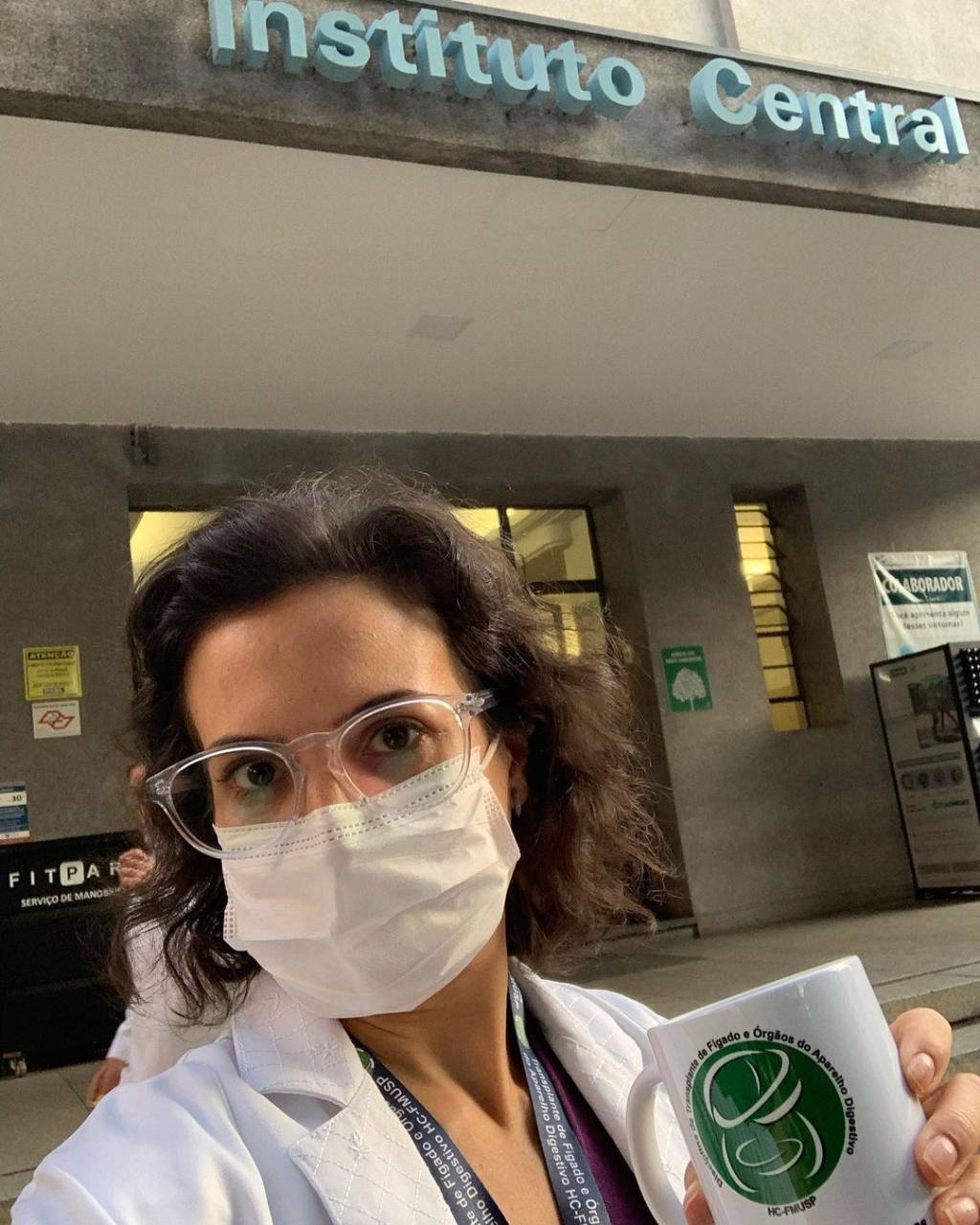 Imagem da médica usando máscara e segurando uma caneca com um logo do Hospital das Clínicas