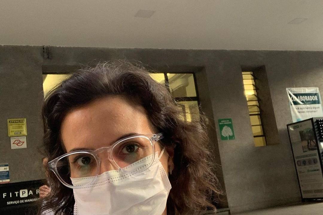 Imagem da médica usando máscara e segurando uma caneca com um logo do Hospital das Clínicas