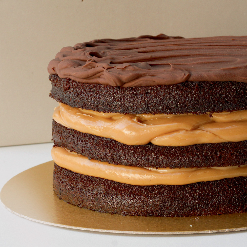 Visão lateral de um bolo dividido em camadas, recheado por doce de leite, com ganache em seu topo e massa escura
