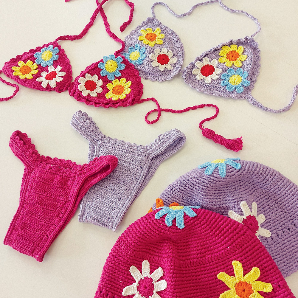 Foto mostra dois conjuntos de biquíni de crochê, um roxo e outro rosa. Eles têm flores.