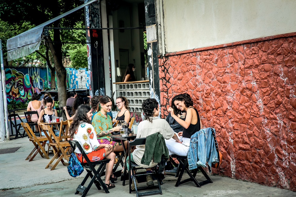 Pessoas sentam-se em mesas de madeira na calçada de uma cervejaria.