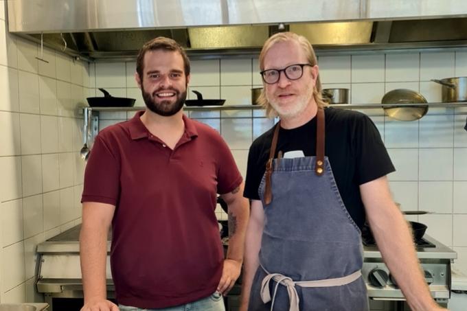 Cesar Costa e Daniel Burns posam lado a lado em cozinha