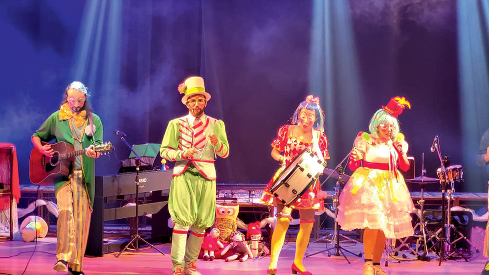 Quatro atores vestem roupas coloridas e tocam instrumentos em um espetáculo infantil