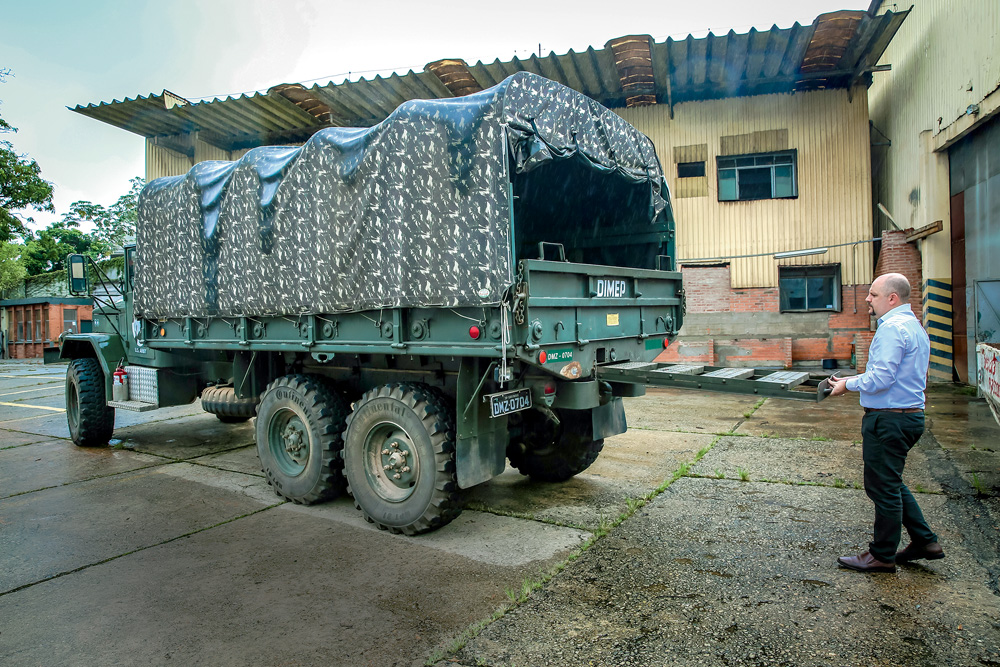 Imagem mostra caminhão militar verde estacionado em pátio.