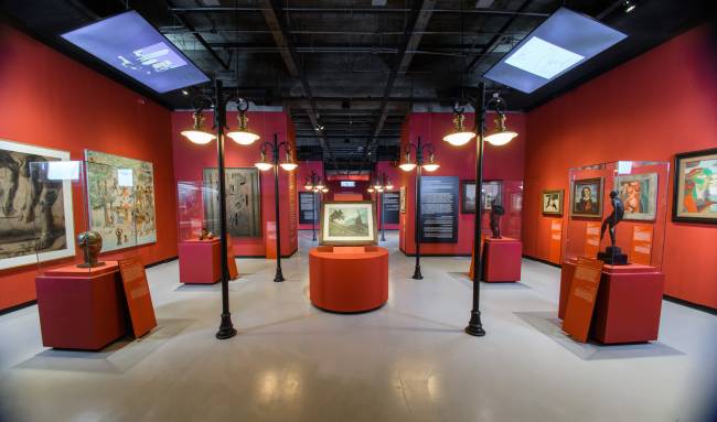 Exposição Farol SantanderIdentidades 1922Foto: Germano Lüders19/02/2022 Espaço expositivo com parede vermelhas, telas nas paredes e em tótens e postes de luz antigos cenográficos