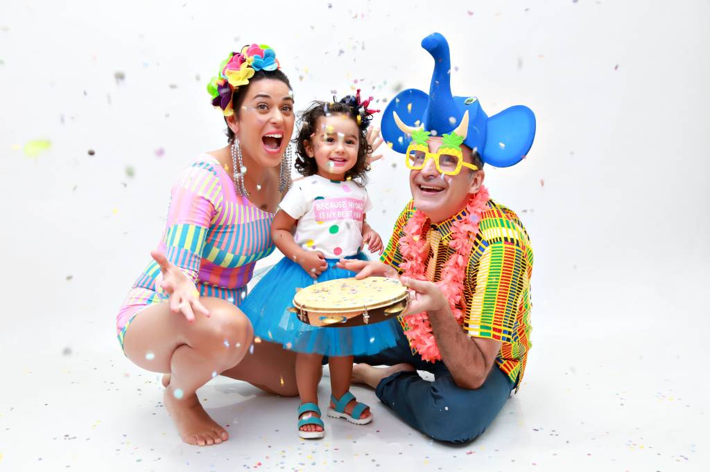 Um homem e uma mulher com roupas de Carnaval ao lado de uma menina com fantasia de princesa