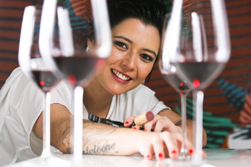 Gabriela Monteleone posa sorridente entre taças de vinhos